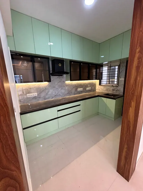 Sage-green L-shaped modular kitchen framed by walnut